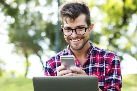 Homem de camisa xadrez ao celular com laptop