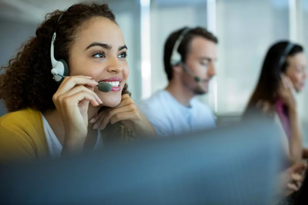 Mulher em uma sala com outas duas pessoas, utilizando o microfone e fone para falar