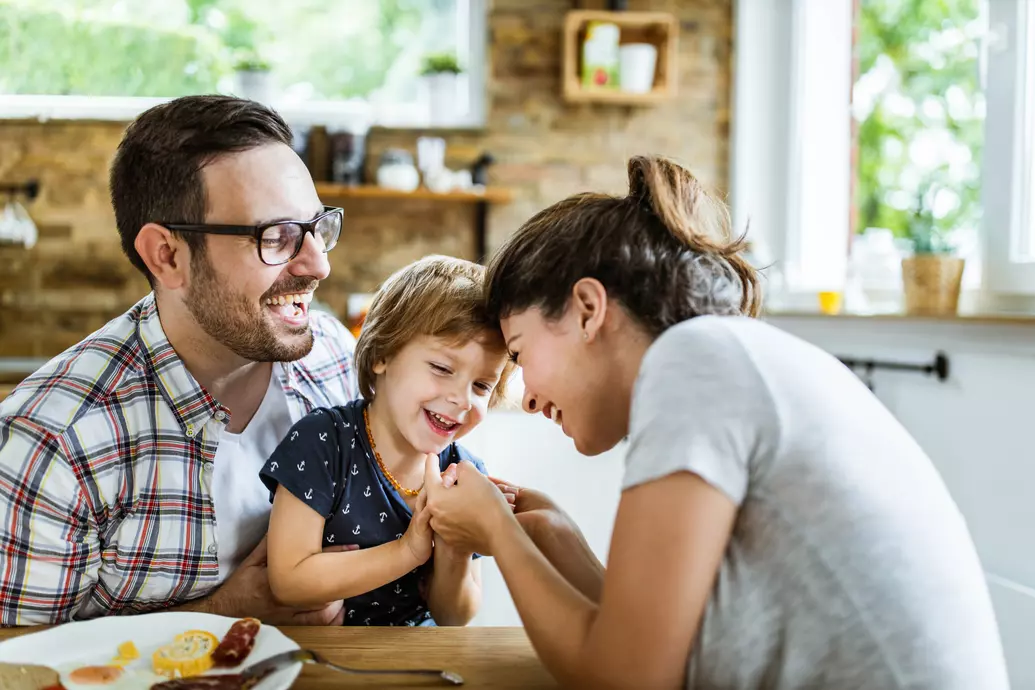 Homem e mulher sentados à mesa brincando com filho